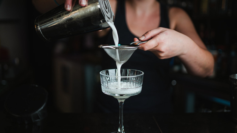 A person double-straining a cocktail into a cocktail glass