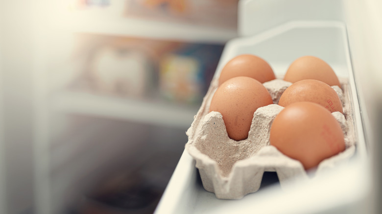 A close-up of an egg carton in a refrigerator containing five brown eggs