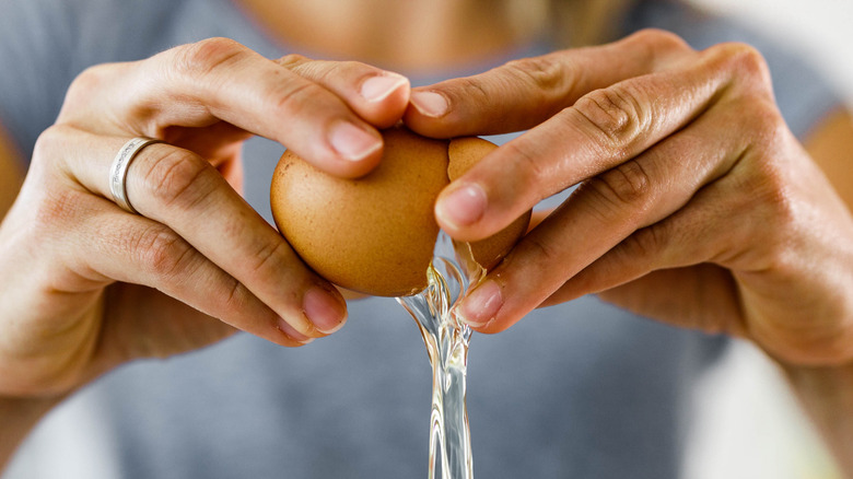 A close-up of someone cracking a brown egg