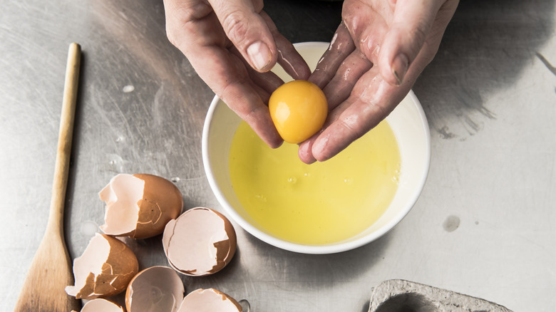 Hands holding an egg yolk above a bowl of egg whites