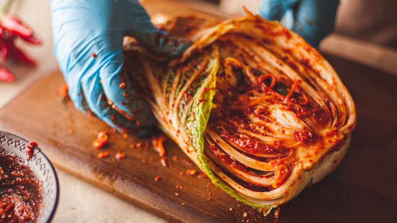 gloved hands rubbing paste on cabbage