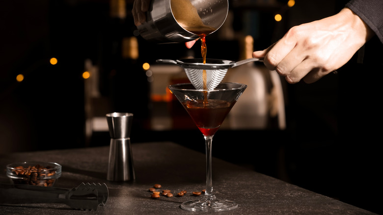 Bartender pouring espresso martini through sieve in bar