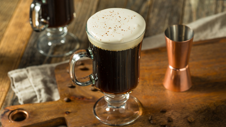 Irish coffee with whipped cream and whiskey on wooden board