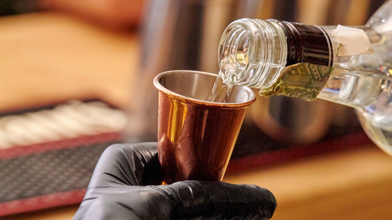 a close-up of a person filling a measuring jigger from a bottle