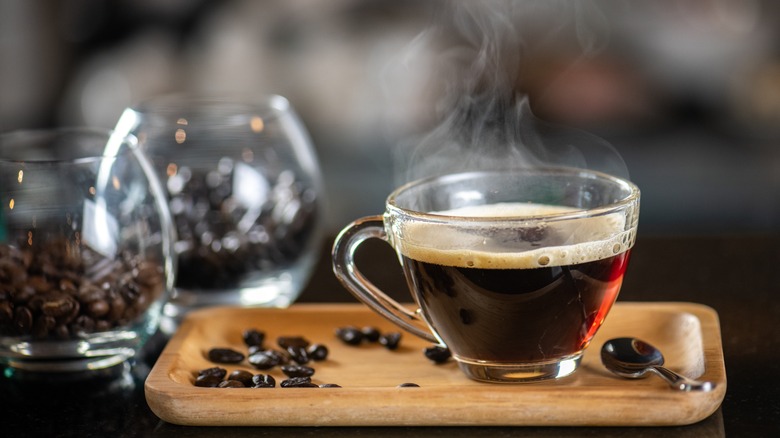 steaming coffee cup on wooden board with cups full of coffee beans