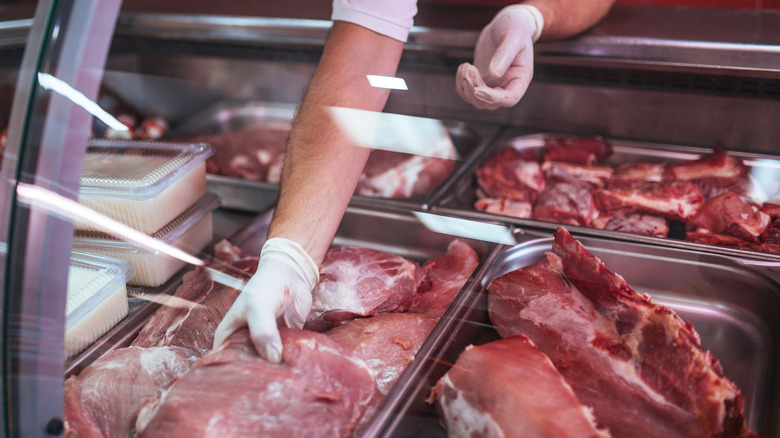 gloved hand reaching toward a variety of meat in the butcher shop meat case