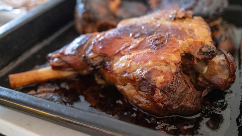 A close-up of a perfectly braised lamb shank, resting in its juices