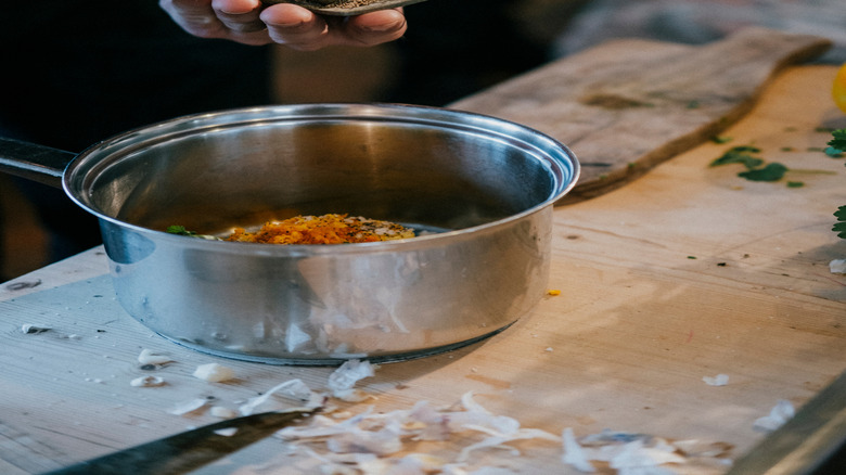 hands adding small spoonfuls of ground spices to a pot