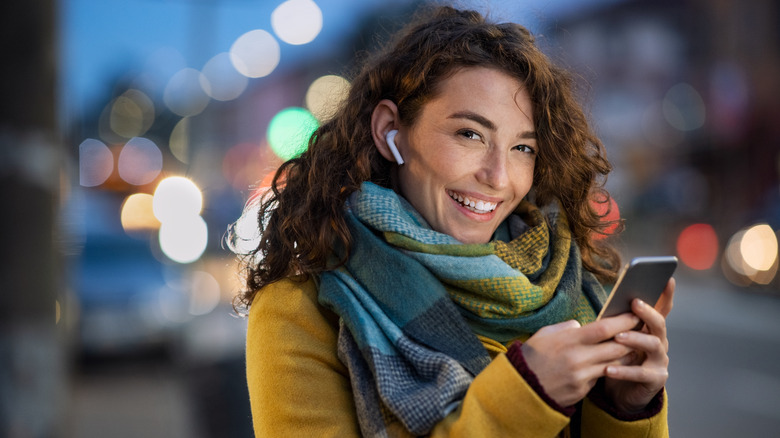 Smiling woman with earbuds, phone