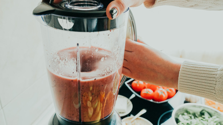 hands holding blender with tomatoes