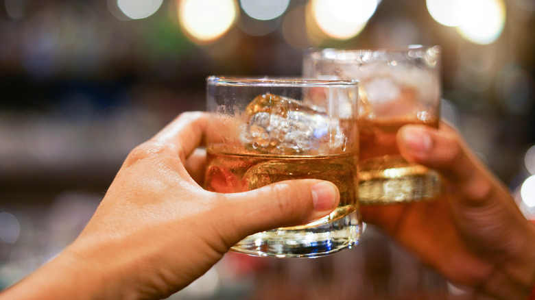 a close-up of hands toasting with glasses of whiskey