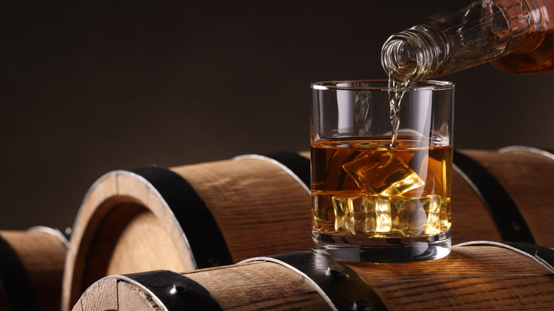 bourbon being poured into a glass on top of oak barrels