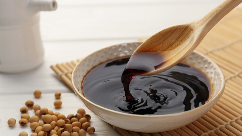 soy sauce in white dotted bowl and wooden spoon with placemat and soy beans