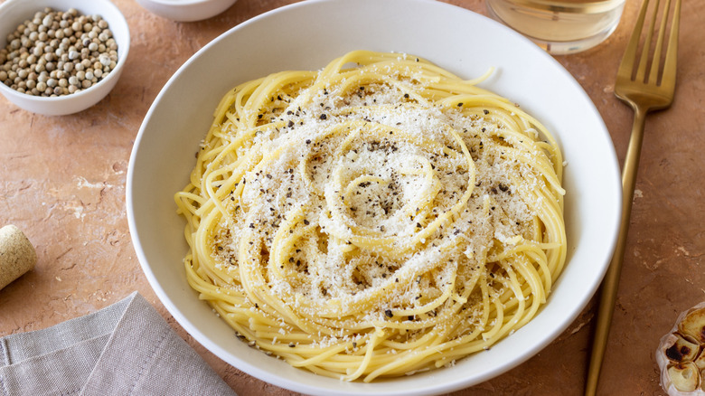 Bowl of cacio e pepe shown with peppercorns and fork