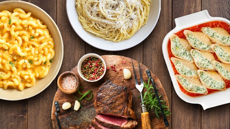 Steak on cutting board surrounded by pasta dishes