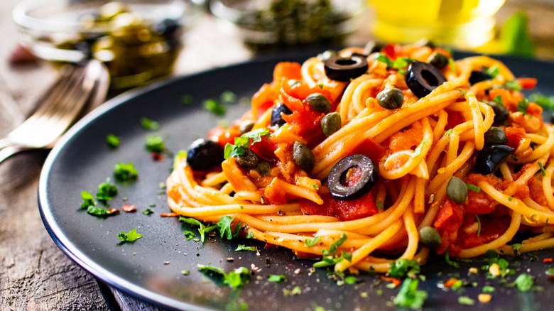 Spaghetti with puttanesca sauce on black plate