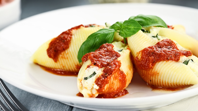 Stuffed pasta shells and fresh basil leaf on white plate