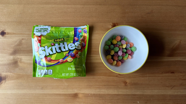 Sour Skittles bag with bowl on wooden table