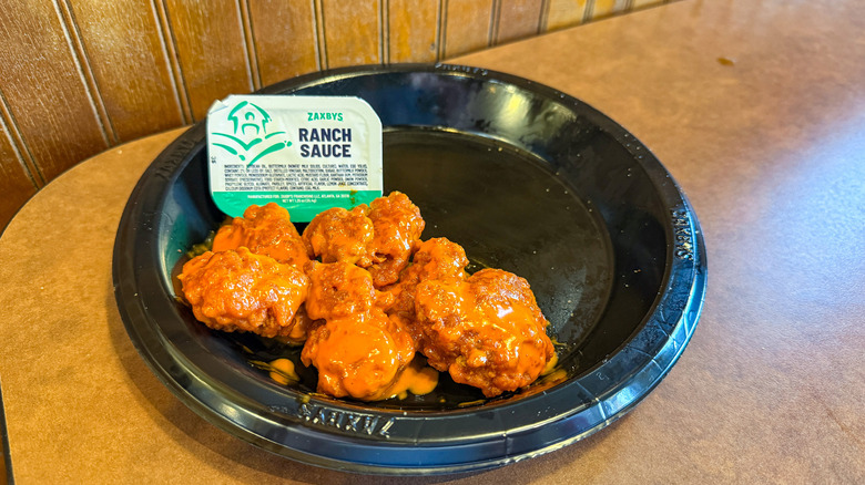 Sauce-covered bonleess wings on black paper plate