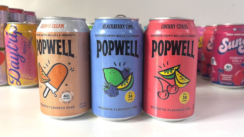 Three Popwell soda cans lined up on white table