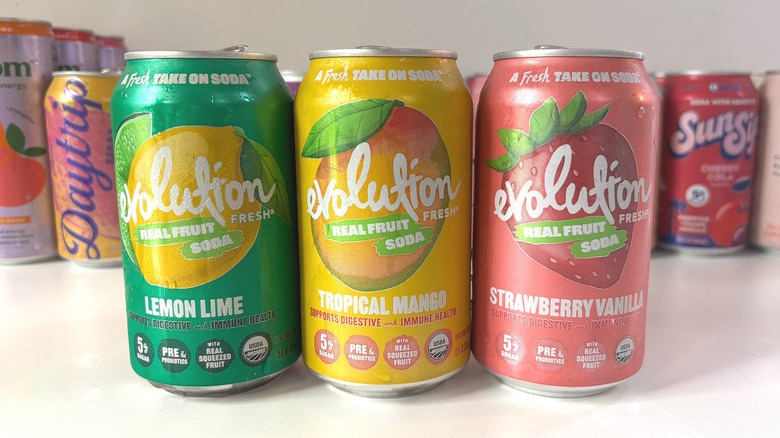 Three Evolution soda cans lined up on white table