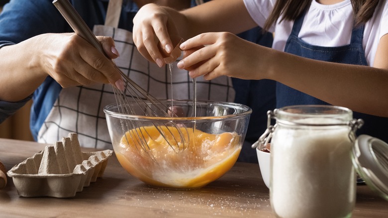 People cracking eggs into bowl