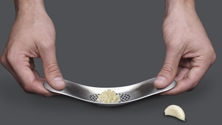 A person pressing garlic with a Joseph Joseph garlic rocker