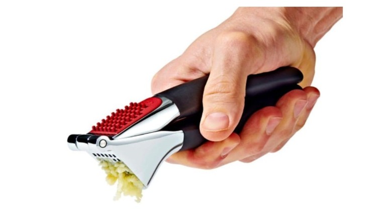 A person pressing a garlic clove with an OXO garlic press