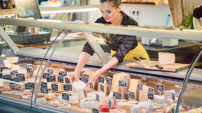 Server picking out a cheese from a display counter of cheeses at a deli