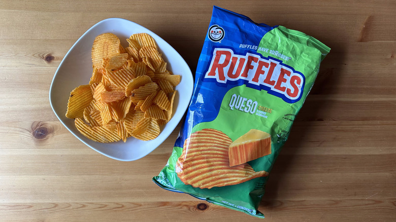 Queso Cheese Ruffles bag with a bowl of chips on a wooden table