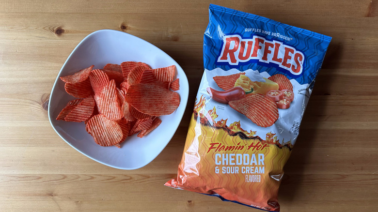Flamin' Hot Cheddar and Sour Cream Ruffles bag with a bowl of chips on a wooden table