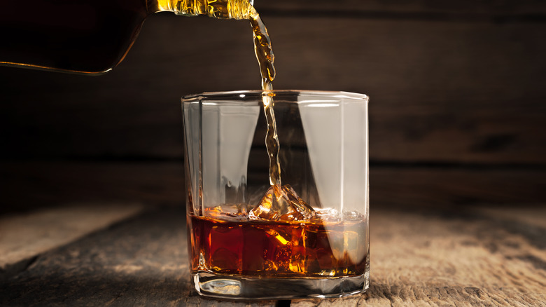 whisky being poured over ice in a glass