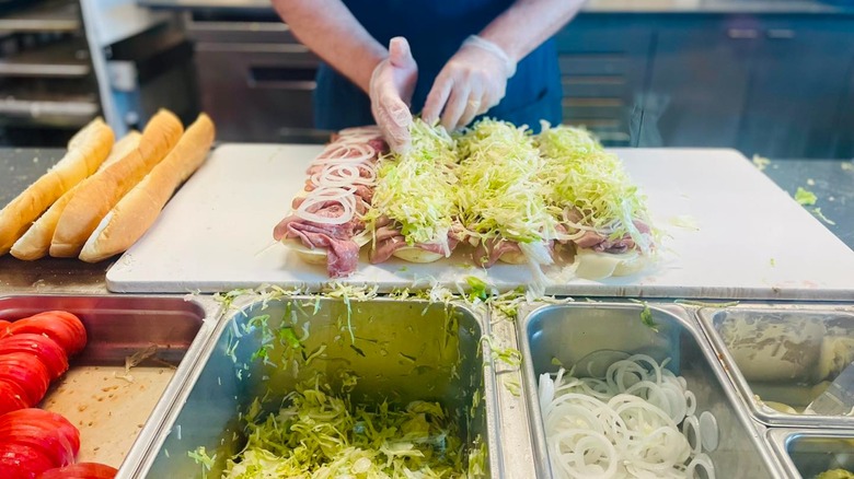 Employee loading up subs with toppings