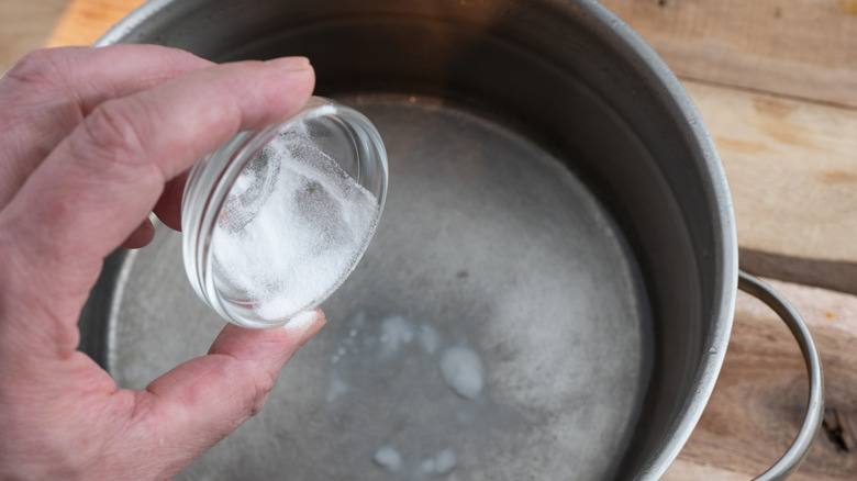 Person adding baking soda to pot of boiling water
