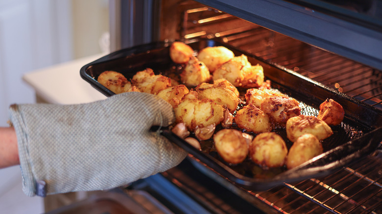 Person taking tray of roasted potatoes out of oven with oven glove