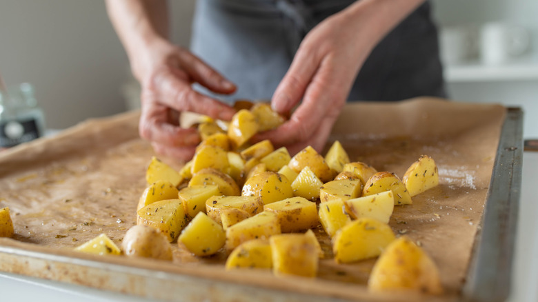 Person arranging chunks of seasoned potatoes on lined baking tray