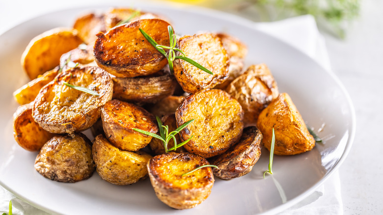 Pile of roasted potatoes with rosemary on white plate