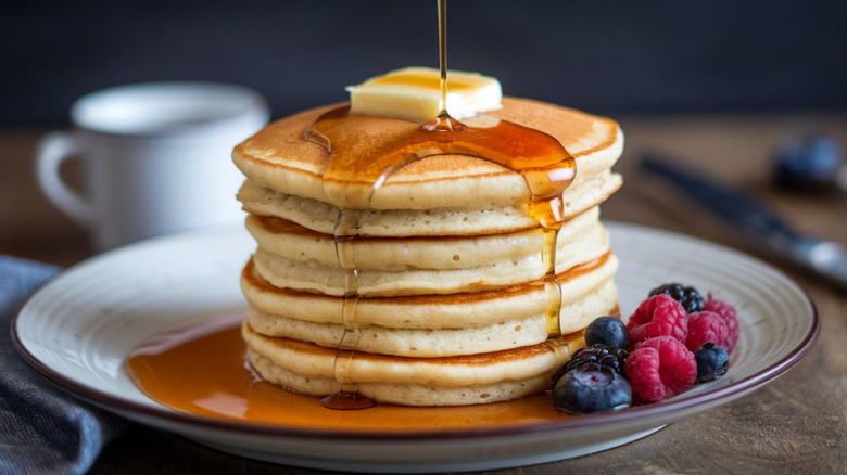 syrup pouring onto fluffy buttermilk pancakes with butter and fresh berry garnish