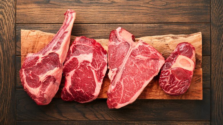 four raw prime steaks on natural wood board on wooden table