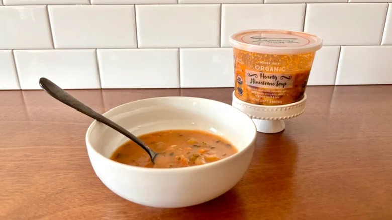 Bowl and container of Trader Joe's Hearty Minestrone soup on a wooden table