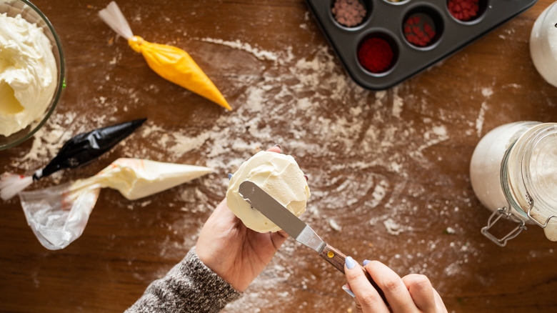 Person scraping icing down side of cupcake