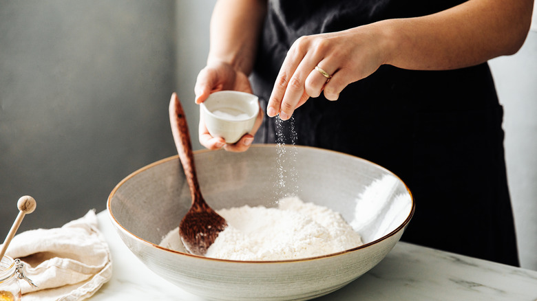 A person sprinkling salt into a bowl of flour