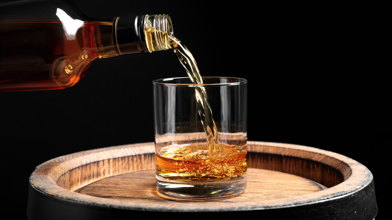 Whiskey poured into a glass on top of a barrel