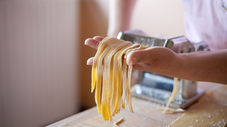 A person holding pasta strands that have come out of the pasta rolling machine