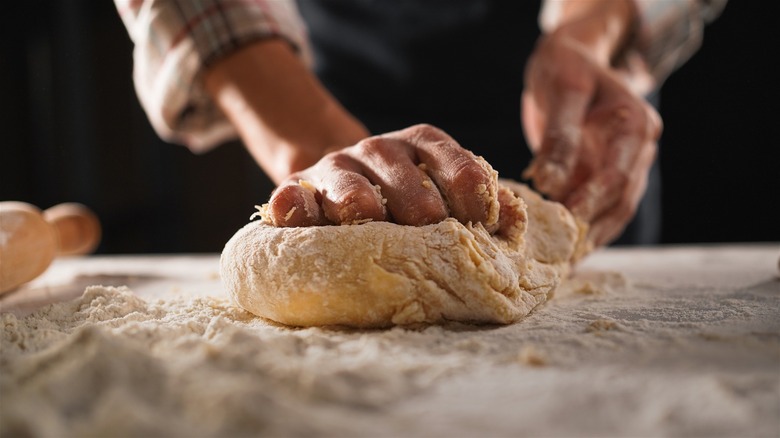 A close-up of two hands kneading pasta dough on a flour-dusted surface