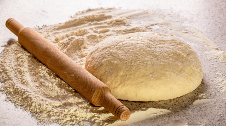 Freshly made pasta dough resting on a flour-dusted kitchen counter next to a wooden rolling pin