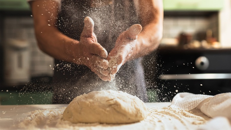 A person standing at the kitchen counter slapping flour-covered hands over a freshly made pasta dough