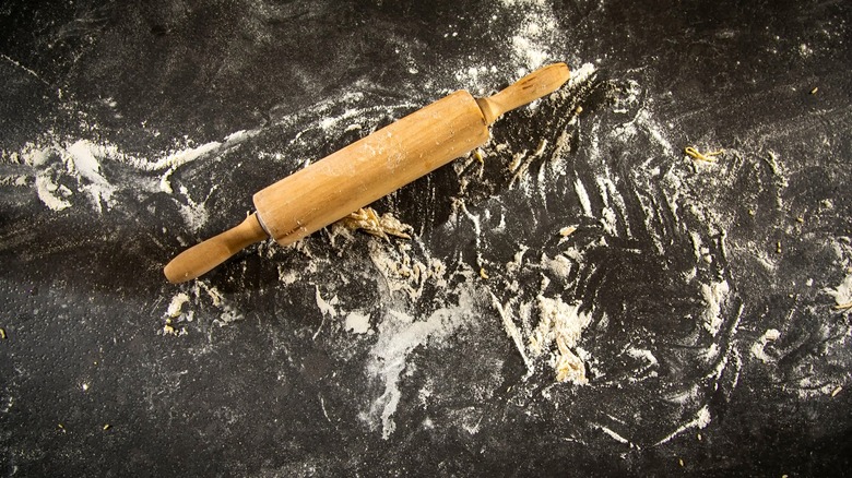 Wooden rolling pin placed on a black counter dusted with flour and dough trimmings