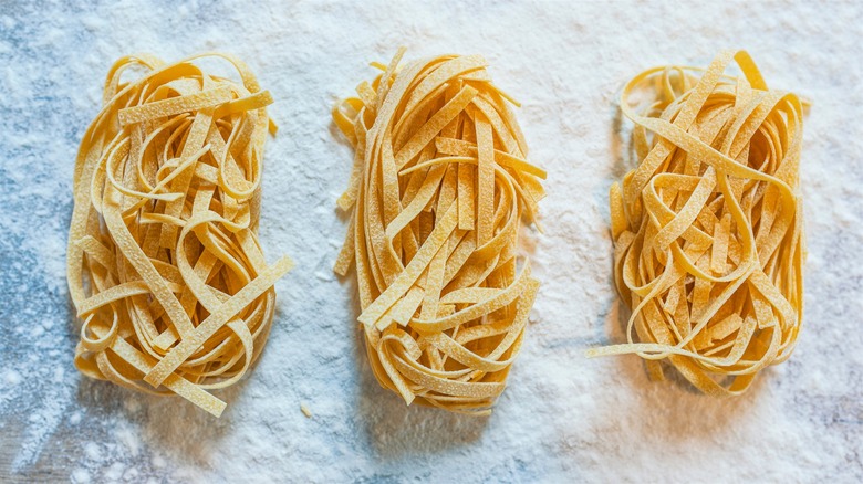 Three palm-sized bundles of homemade fettuccine pasta resting on a floured blue-colored counter