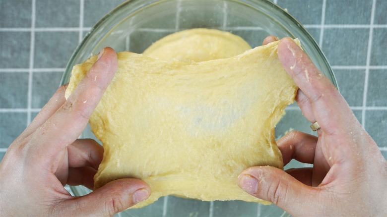 A person stretching out freshly made dough that is sitting in a glass bowl, using the classic windowpane test